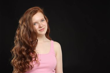 Siyah arka planda sağlıklı dalgalı saçları olan güzel bir genç kız. Metin için boşluk