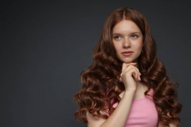 Koyu gri arka planda sağlıklı dalgalı saçları olan güzel bir genç kız. Metin için boşluk