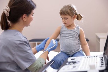 Sonograf klinikte küçük bir kızın kolunun ultrason muayenesini yapıyor.