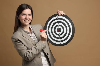 Hedef alınıyor. Dart tahtası ve bej arka planda oku olan gülümseyen iş kadını.