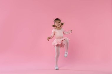 Pembe arka planda dans eden tatlı küçük kız.