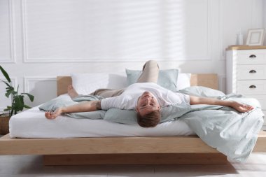 Genç adam evde yumuşak bir döşekle yatakta yatıyor.