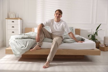 Genç adam evinde yumuşak bir yatakla yatakta oturuyor.