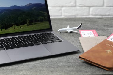 Pasaportlar, uçuş biletleri, uçak modeli ve laptop gri masada, yakın plan.