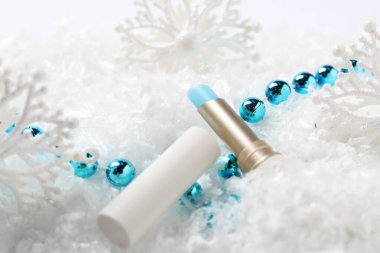 Nemlendirici dudak kremi ve yapay kar üzerine Noel süsü, yakın plan. Kış bakımı