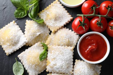 Pişmemiş ravioli, sos, domates ve fesleğen siyah masada, düz yerde.