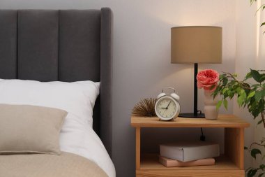 İçinde lamba, çalar saat, kitaplar ve yatağın yanında dekor olan komodin. İç tasarım