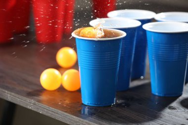 Bira pong oyunu. İçkili plastik bardaklar ve toplar ahşap masada, yakın plan.