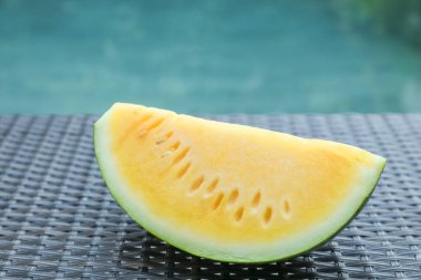 Açık havuz kenarında hasır masada lezzetli bir karpuz dilimi, yakın plan.