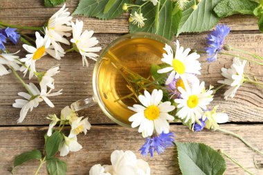 Cam bardakta Aromatik bitki çayı, tahta masada çiçekler ve yeşil yapraklar, düz uzanmış