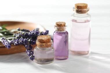 Beyaz ahşap masada doğal yağ ve lavanta çiçekleri, yakın plan.