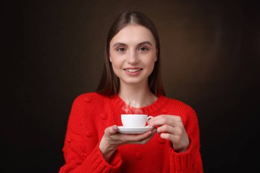 Kahverengi arka planda bir fincan kahveyle gülümseyen kadın.