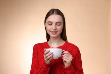 Bej renkli arka planda bir fincan kahveyle gülümseyen kadın