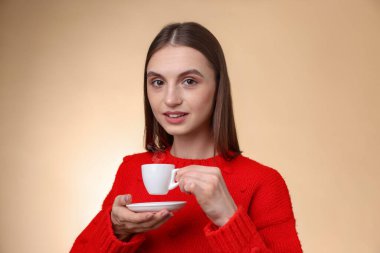 Bej renkli arka planda fincandan kahve içen kadın