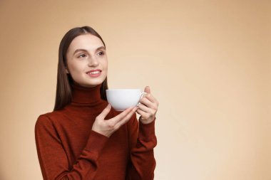 Bej renkli arka planda bir fincan kahveyle gülümseyen kadın. Metin için boşluk