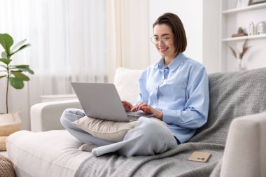 Ofisteki kanepede dizüstü bilgisayarla çalışırken gülümsemek.