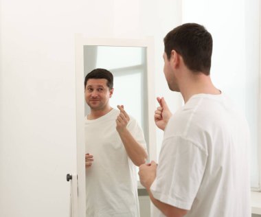 Yakışıklı adam aynanın yanında kalp hareketi gösteriyor.