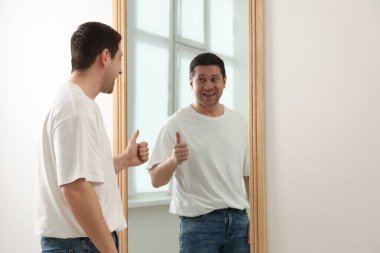 Kapalı alanda aynanın yanında baş parmağını gösteren yakışıklı adam.