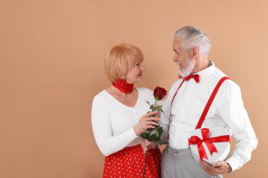 Hediye kutusu ve açık kahverengi arka planda gül olan sevimli son sınıf çifti, mesaj için yer var.