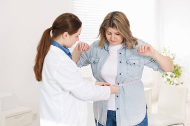 Kilo kaybı. Klinikte kilolu bir kadının belini bantla ölçen beslenme uzmanı.