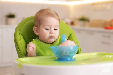 Küçük şirin bebek, yüksek sandalyede sağlıklı yiyecekler yiyor.