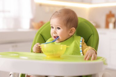 Küçük şirin bebek, yüksek sandalyede sağlıklı yiyecekler yiyor.