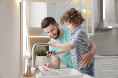 Baba ve oğlu evde birlikte bulaşık yıkıyorlar.