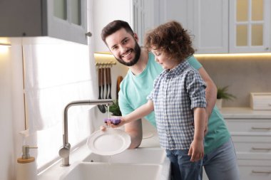 Baba ve oğlu evde birlikte bulaşık yıkıyorlar.