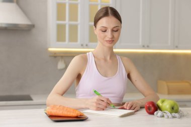 Beyaz ahşap masada beslenme planı geliştiren bir kadın.