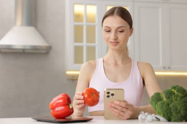 Beyaz masadaki akıllı telefon ve domatesli kadın.