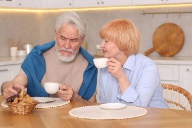 Mutfaktaki ahşap masada birlikte kahvaltı eden sevimli yaşlı çift.