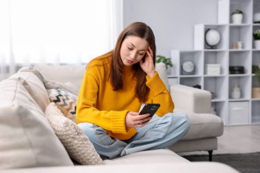 Evdeki kanepede akıllı telefon kullanan genç bir kız.