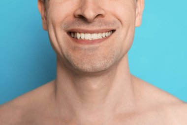 Açık mavi arka planda tıraş olduktan sonra gülümseyen adam, yakın plan.