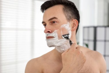 Yakışıklı adam evde aynanın yanında tıraş oluyor.