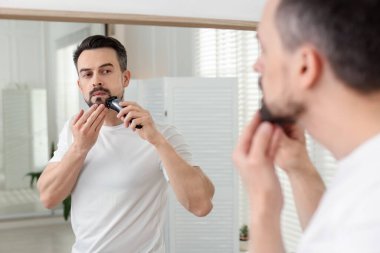 Yakışıklı adam evde aynanın yanında tıraş makinesiyle tıraş oluyor.