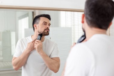 Yakışıklı adam evde aynanın yanında tıraş makinesiyle tıraş oluyor.