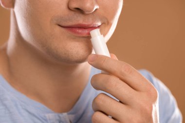 Genç adam dudaklarına krem sürüyor açık kahverengi arka planda, yakın plan.