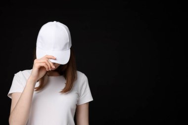 Siyah arka planda şık beyaz beysbol şapkası takan genç bir kadın.