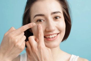 Açık mavi arka plana kontak lens takan kadın, yakın plan