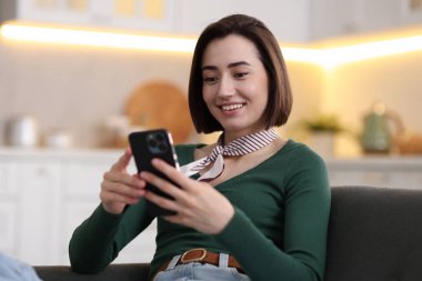 Evdeki koltukta modern akıllı telefon kullanan bir kadın.