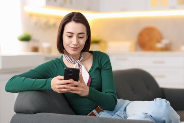 Evdeki koltukta modern akıllı telefon kullanan bir kadın. Metin için boşluk