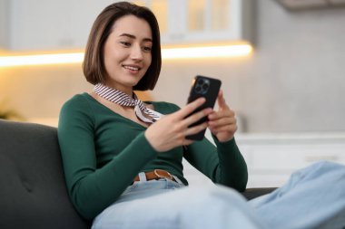 Evdeki koltukta modern akıllı telefon kullanan bir kadın.