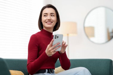 Evdeki koltukta modern akıllı telefon kullanan bir kadın.