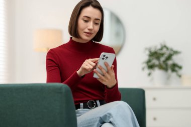 Evdeki koltukta modern akıllı telefon kullanan bir kadın.