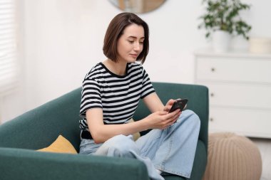 Evdeki koltukta modern akıllı telefon kullanan bir kadın.