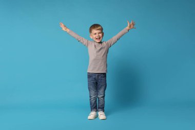 Mutlu küçük çocuk açık mavi arka planda dans ediyor