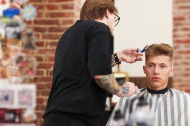 Profesyonel berber berber dükkanında müşterinin saçını makasla kesiyor.