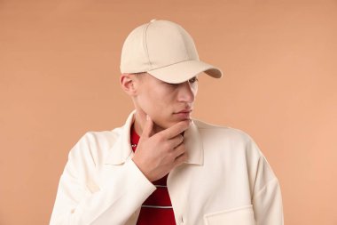 Beyzbol şapkalı genç adam bej arka planda.