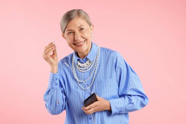 Kulaklıklı yaşlı kadın pembe arka planda müzik dinliyor.