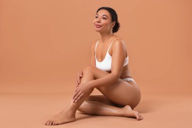 Beyaz iç çamaşırlı, pürüzsüz bir kadın. Bej arka planda epilasyon işleminden sonra.